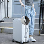 Person holding a white suitcase with a cat carrier on top, standing outside a building.