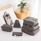 Set of gray packing cubes and bags on a bed with a plant in the background