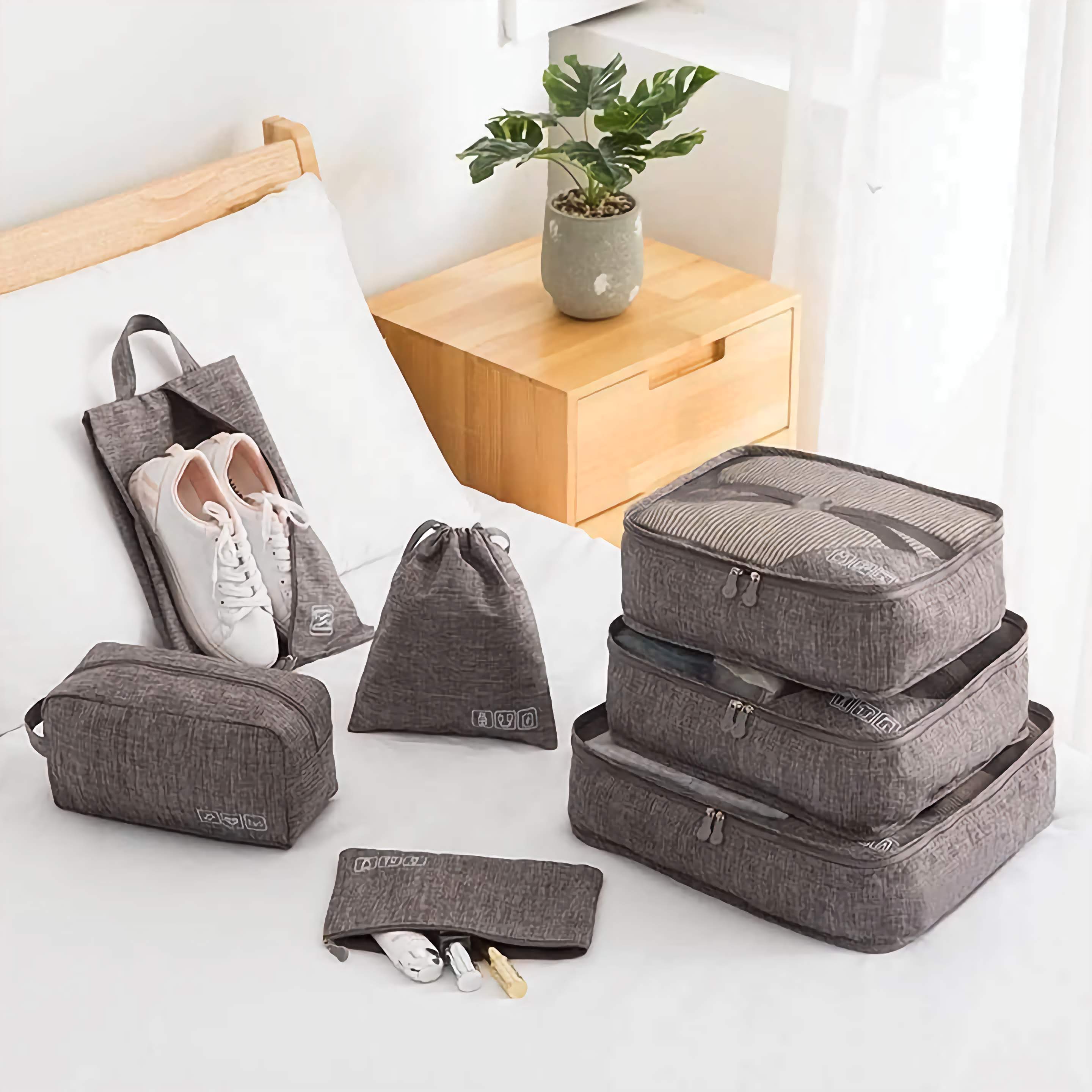 Set of gray packing cubes and bags on a bed with a plant in the background